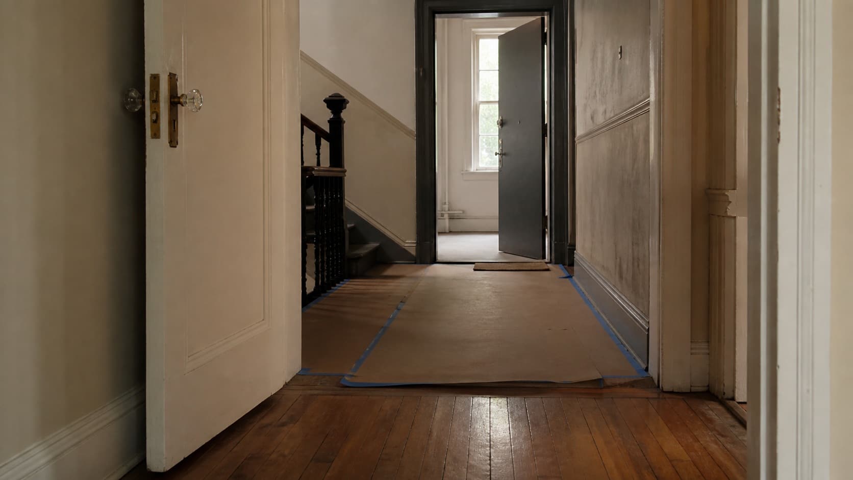 A New York apartment hallway with a wood floor and a service door standing open