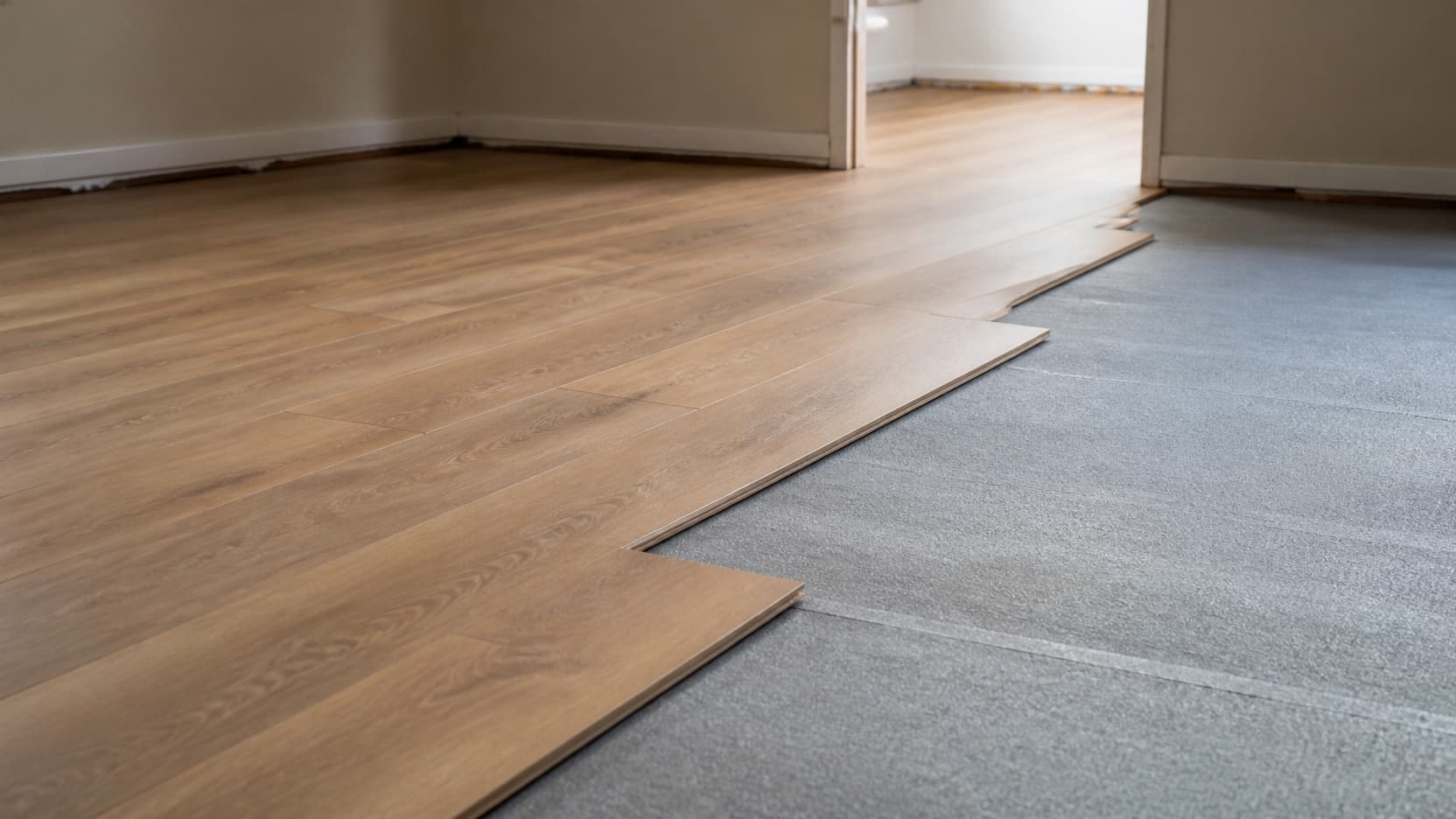 Laminate planks being clicked together over underlay in an empty room
